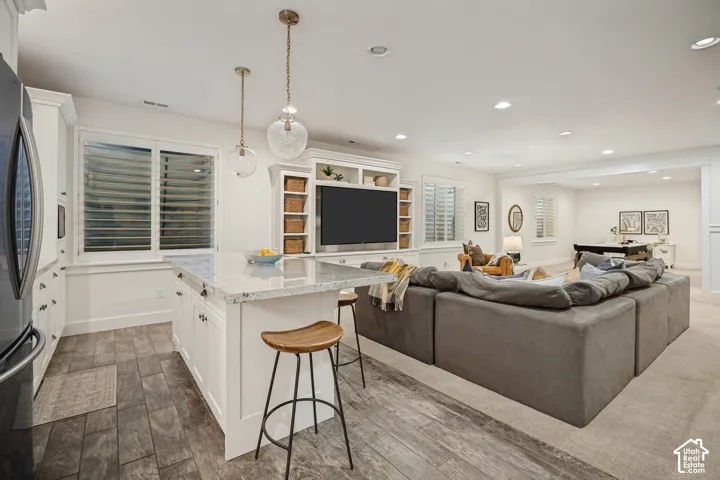Open-concept living area with a white kitchen island featuring a granite-style countertop, recessed lighting, and wood-finish flooring