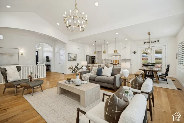 Vaulted ceiling with a chandelier, wood-finish flooring, white kitchen cabinetry, and plantation shutters