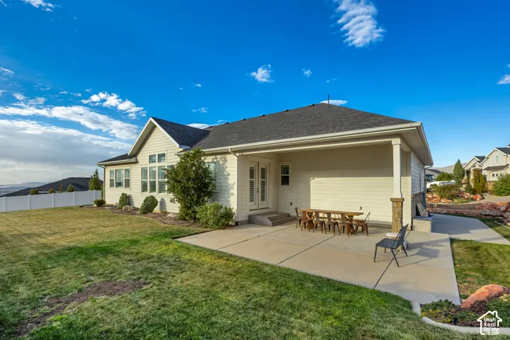 Expansive rear yard with a manicured lawn, white fencing, and a covered patio with a stone-clad pillar