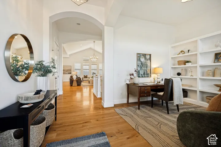 Hardwood flooring, arched entryway, built-in shelving, vaulted ceiling, and recessed lighting