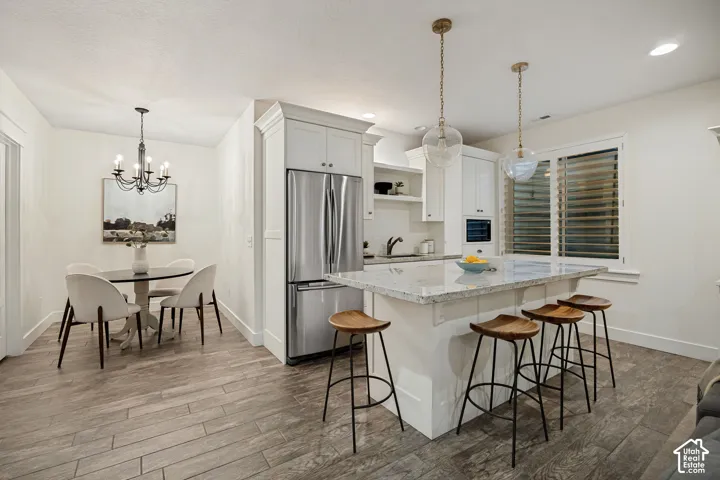 Open-concept kitchen featuring white cabinetry, stainless steel appliances, a large island with a light-toned countertop, and wood-finish flooring