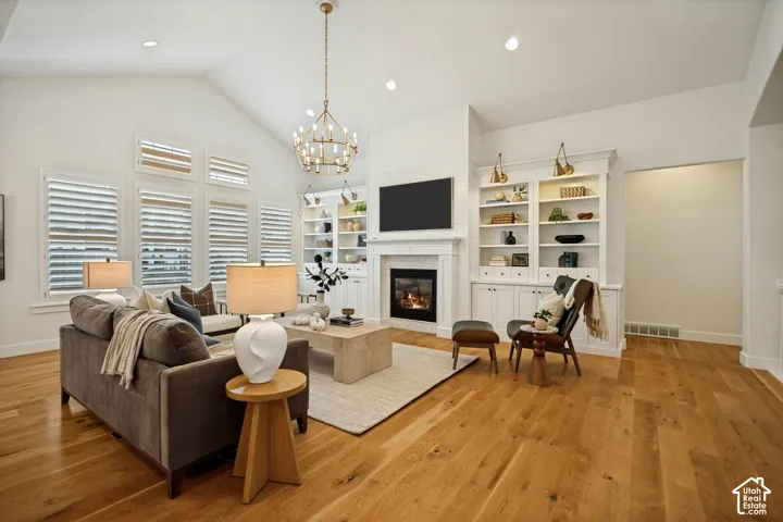 Vaulted ceiling with a contemporary chandelier, recessed lighting, wood-finish flooring, built-in shelving, and a fireplace