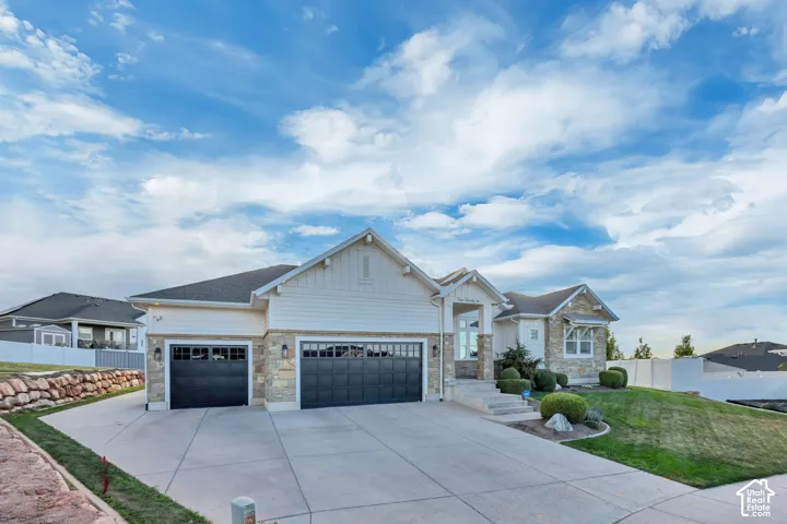 Stone and siding exterior with a multi-car garage, concrete driveway, and front landscaping