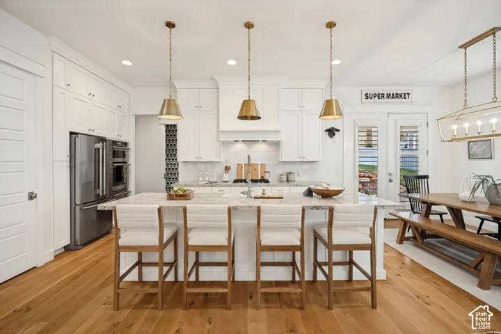 Kitchen featuring white cabinetry, stainless steel appliances, a center island with a light-toned countertop, wood-finish flooring, and pendant lighting