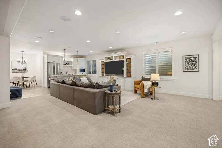 Recessed lighting, light-colored carpeting, built-in media console, white kitchen cabinetry, and stainless steel appliances