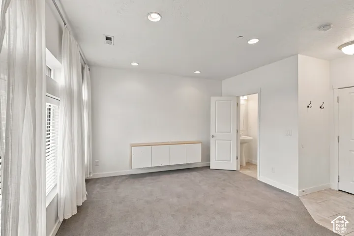 Recessed lighting illuminates this room featuring wall-to-wall carpeting and a window with blinds and sheer drapes
