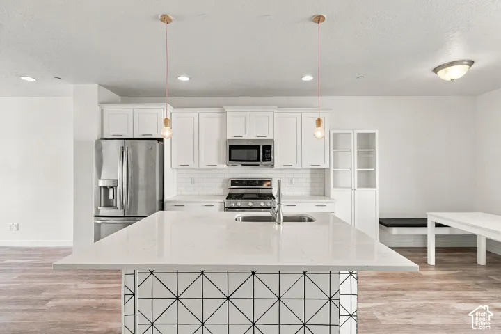 Kitchen featuring a central island with geometric tile detail, white cabinetry, a subway tile backsplash, stainless steel appliances, and wood-finish flooring