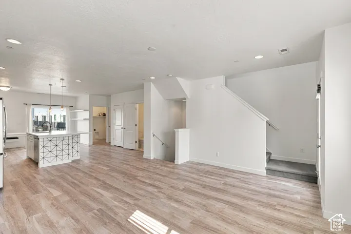 Open-concept living area featuring wood-finish flooring, recessed lighting, a kitchen island with pendant lighting, and a staircase with a carpeted runner