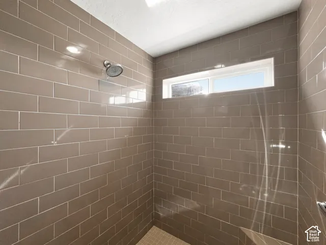 Primary bedroom bathroom featuring tiled shower surround with a fixed showerhead, built-in window, and recessed lighting