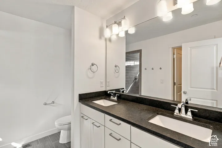 Primary bedroom en suite featuring dual vanity with integrated sinks, dark countertop, white shaker cabinetry, and chrome fixtures