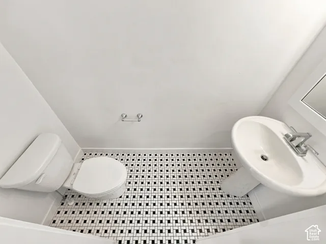 Black and white mosaic tile flooring, white pedestal sink, white toilet, and a wall-mounted mirror