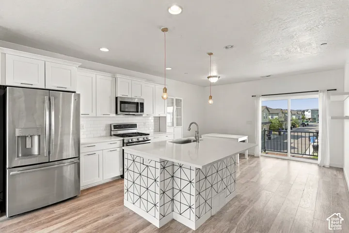 Kitchen featuring white cabinetry, stainless steel appliances, a center island with countertop seating, wood-finish flooring, and a sliding glass door to an exterior balcony