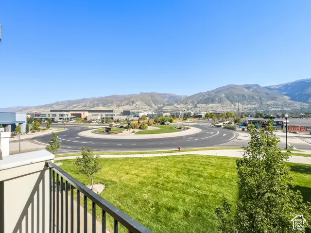 Balcony off living room with metal railing overlooking a landscaped roundabout, green space, and distant mountains