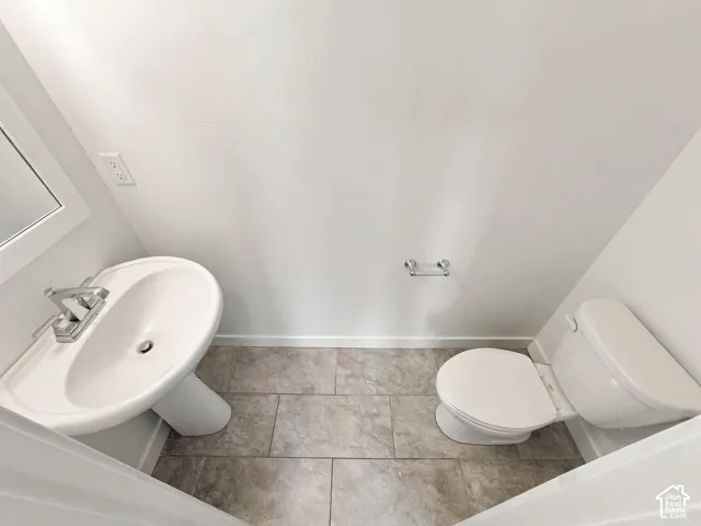 Pedestal sink with chrome faucet, toilet, and tiled flooring