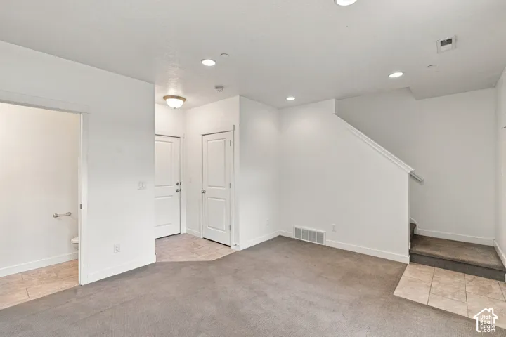 Recessed ceiling lighting, tiled entryway flooring, stairway with carpeted treads, white interior doors, and neutral wall finishes