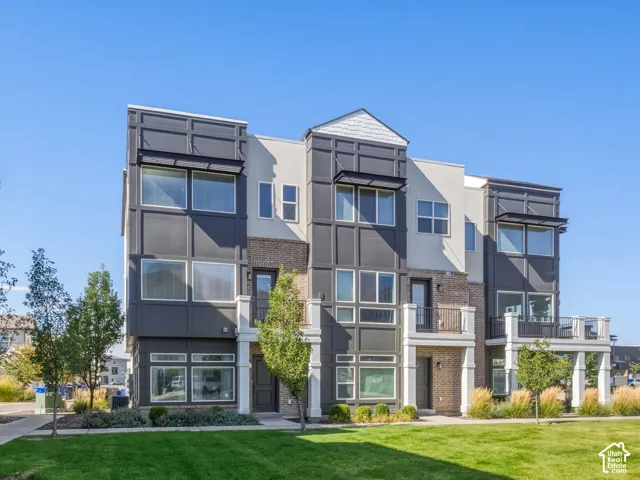 Contemporary townhome architecture featuring a brick facade, large windows, and a private balcony