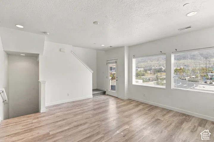 Spacious room featuring wood-finish flooring, recessed lighting, and multiple windows with blinds