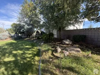 Expansive green lawn, mature trees, concrete block perimeter wall, white fencing, and natural rock landscaping elements