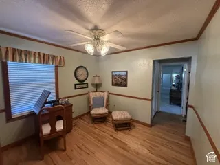 Wood-finish flooring, ceiling fan with light fixture, window with blinds, and decorative trim