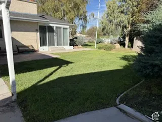 Expansive green lawn, brick exterior, sliding glass doors, concrete patio, mature trees