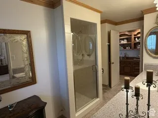 Spa-inspired primary bathroom featuring a frameless glass-enclosed shower with tile surround, dual vanities with wood cabinetry and quartz countertops, a circular mirror with wood framing, and wood-finish flooring throughout