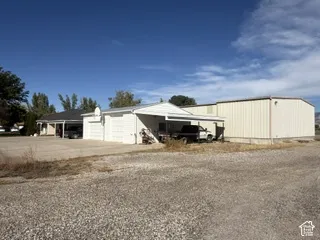 Gravel lot with a detached two-car garage, an attached single carport, and a large metal-sided outbuilding
