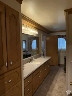 Primary Bathroom featuring dual vanities with stone countertops, wood-finish cabinetry, large framed mirror with integrated lighting, and abundant natural light from multiple windows
