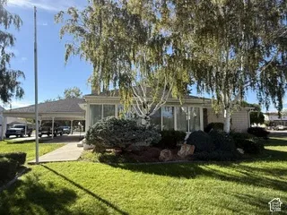 Manicured lawn with mature trees, extensive front landscaping, large windows, and an attached carport