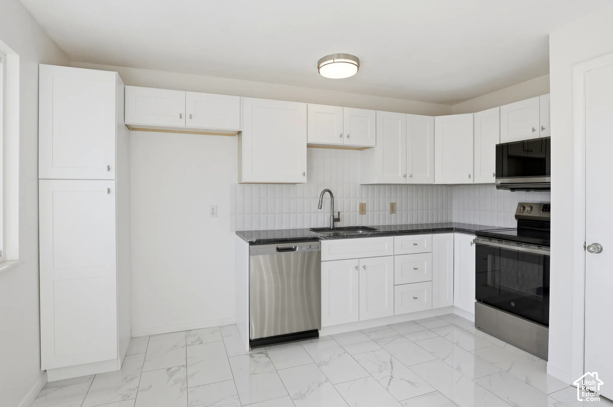Updated kitchen with white cabinetry, black countertops, and stainless steel appliances