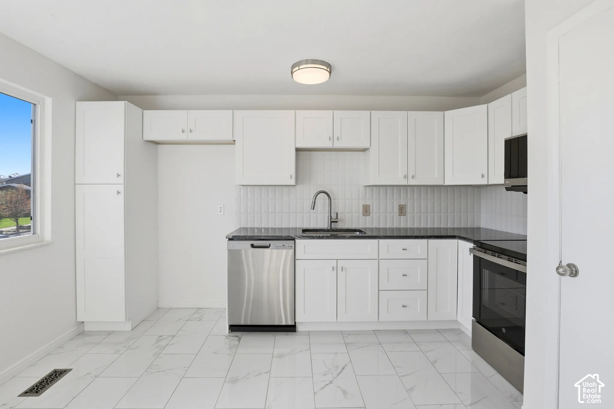 White shaker-style cabinetry, dark countertops, white tile backsplash, and stainless steel appliances