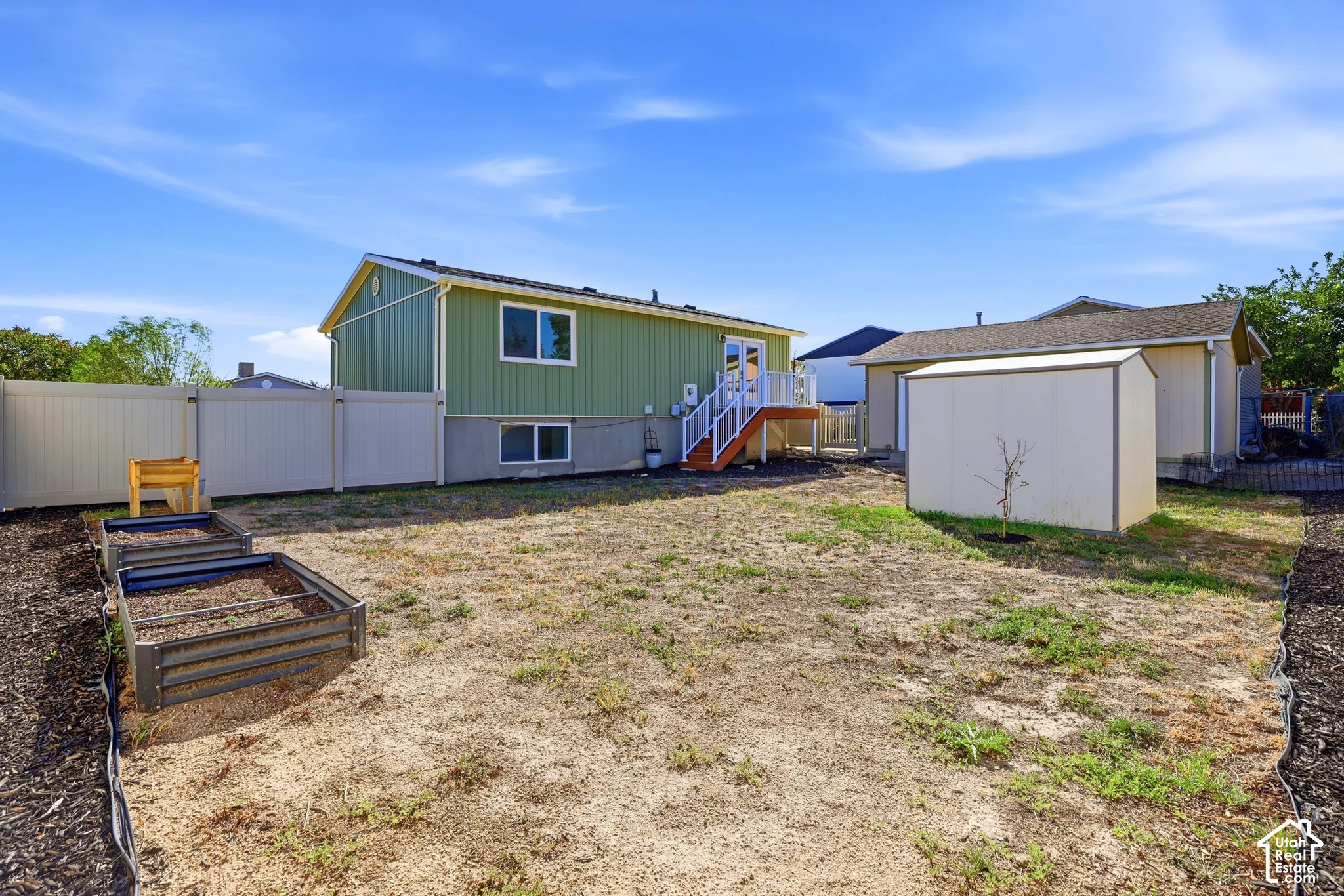Rear exterior featuring a deck with white railings, a detached shed, and raised garden beds