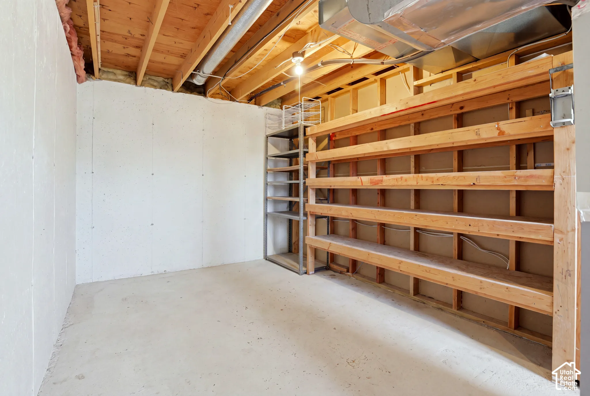 Unfinished basement space featuring exposed wood joists, concrete flooring, and built-in wood shelving