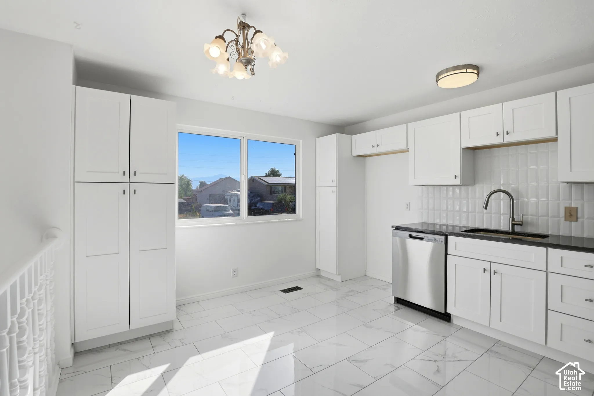 White cabinetry, dark stone countertops, stainless steel dishwasher, white subway tile backsplash, and white tile flooring