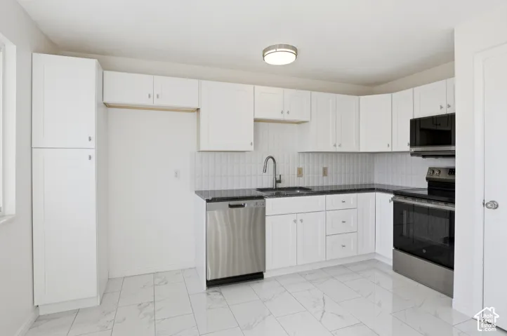 Updated kitchen with white cabinetry, black countertops, and stainless steel appliances