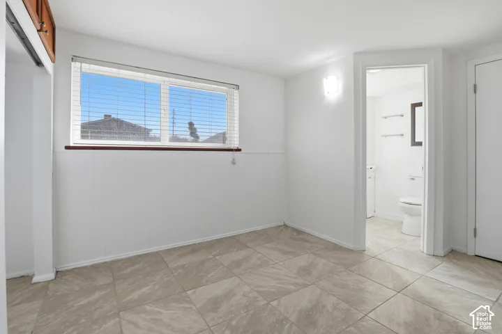 Tile flooring, window with blinds, wall-mounted light fixture, recessed wall paneling, and an interior doorway