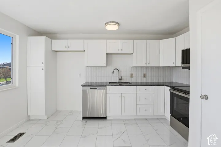 White shaker-style cabinetry, dark countertops, white tile backsplash, and stainless steel appliances