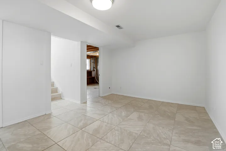 Recessed ceiling light, neutral wall paint, tiled flooring, interior staircase, unfinished utility area