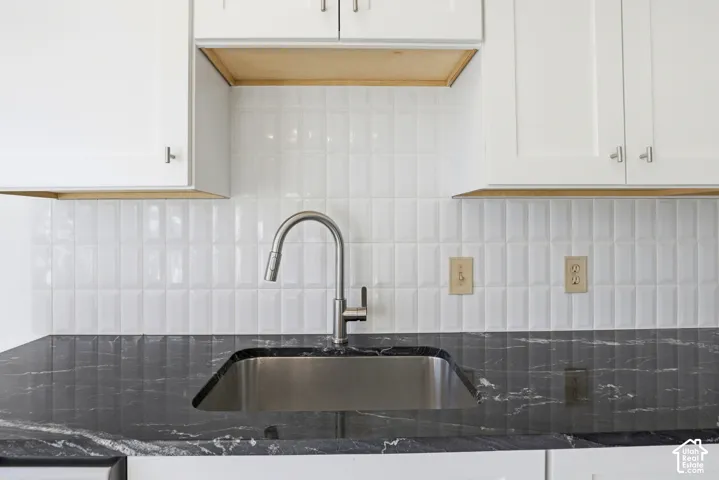 White subway tile backsplash, stainless steel sink, brushed nickel faucet, dark stone countertop, white cabinetry