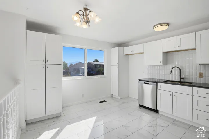 White cabinetry, dark stone countertops, stainless steel dishwasher, white subway tile backsplash, and white tile flooring