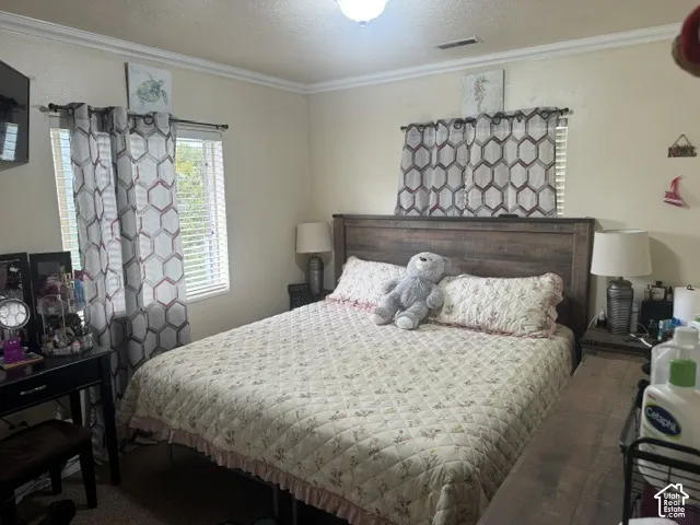 Wood-finish headboard, window with horizontal blinds, textured walls, and crown molding
