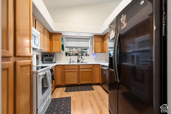 Kitchen featuring wood-finish cabinetry, white countertops, stainless steel refrigerator, white electric range, and wood-finish flooring