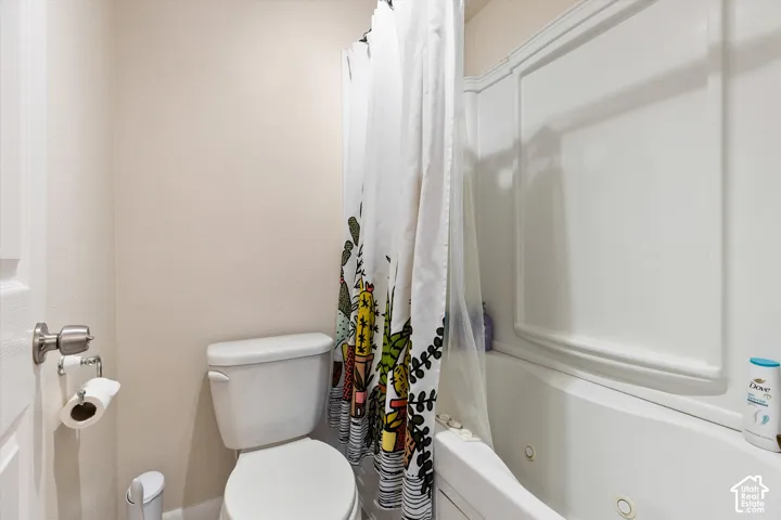 White panel-sided built-in bathtub with a white toilet and a brushed nickel door handle