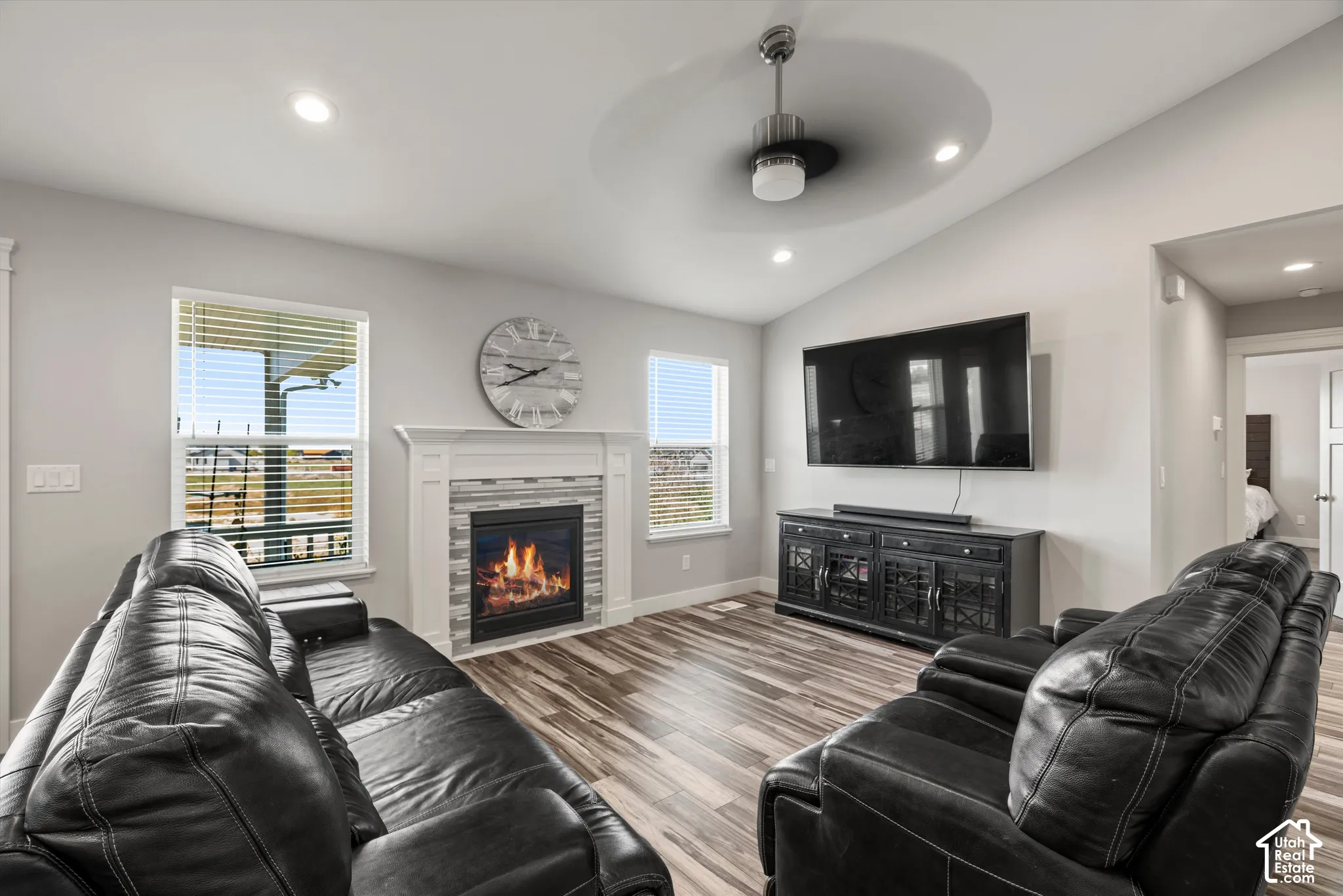 Vaulted ceiling with a ceiling fan, recessed lighting, wood-finish flooring, and a fireplace with a white mantel and tile surround