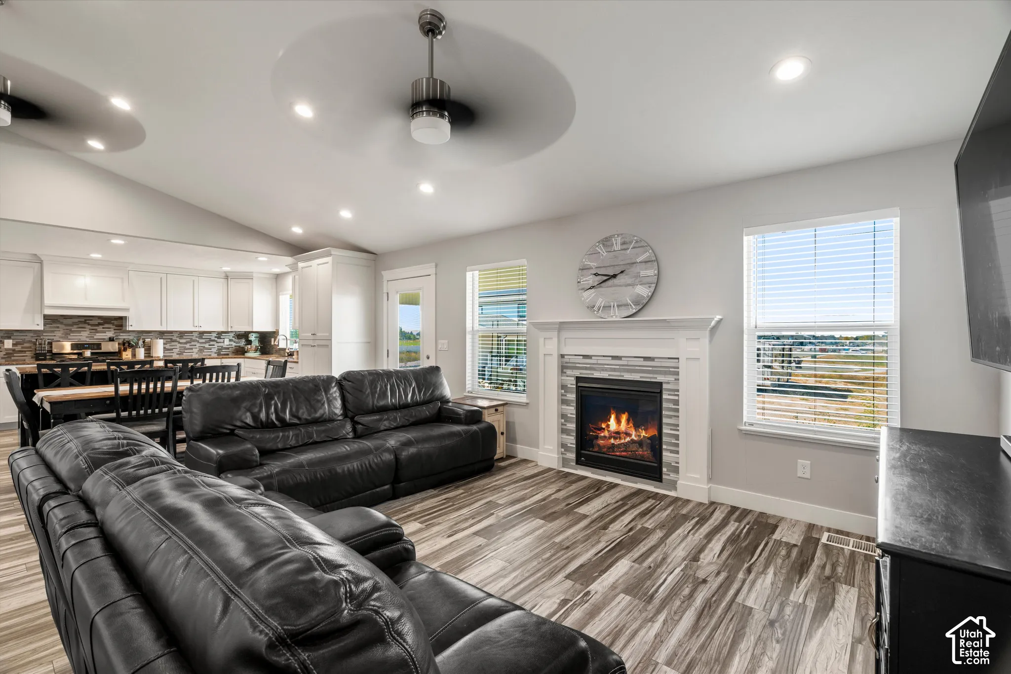 Vaulted ceiling with recessed lighting and two ceiling fans, wood-finish flooring, built-in fireplace with tile surround and mantel, and white cabinetry