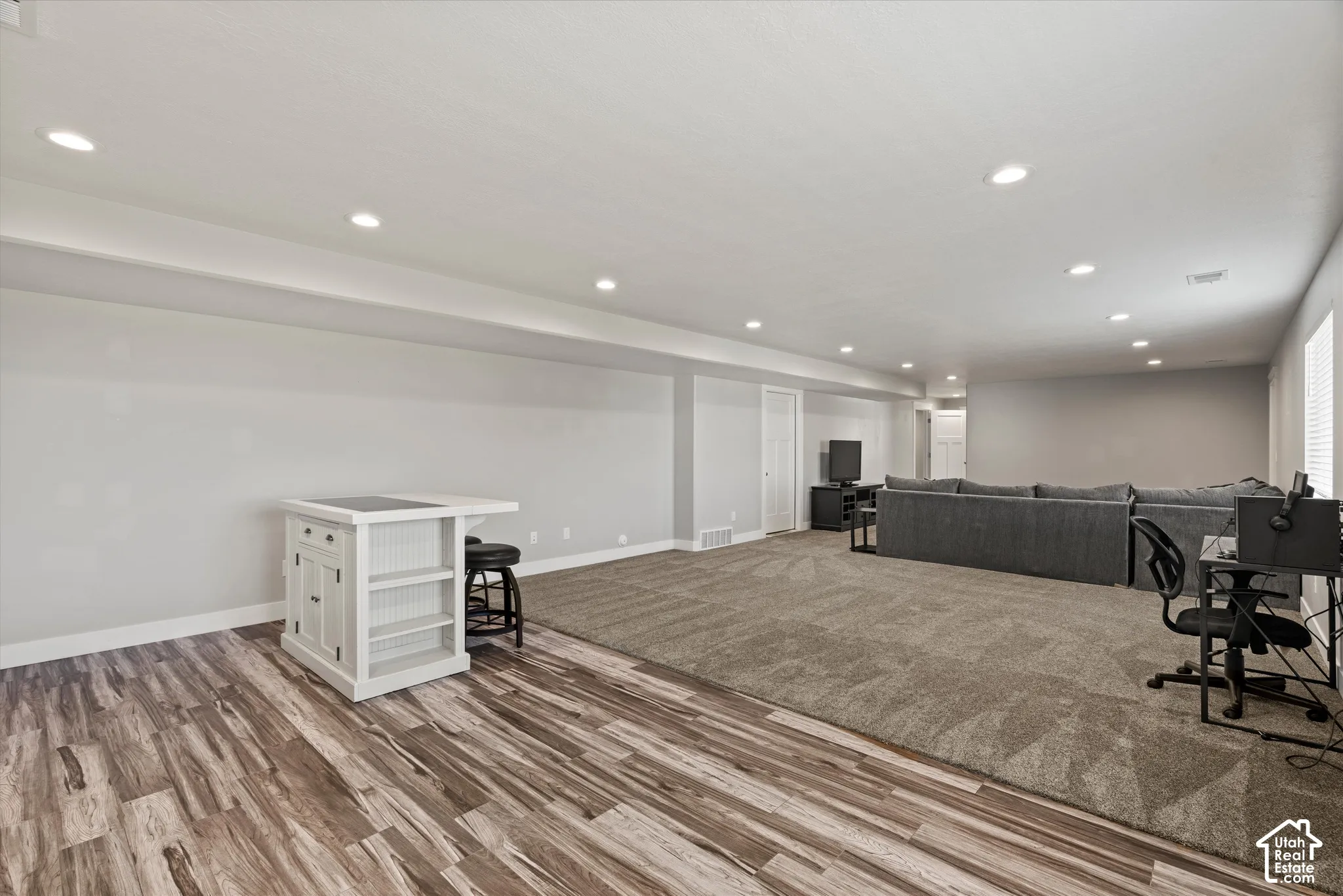 Recessed lighting illuminates this expansive room featuring wood-finish flooring and plush carpeting