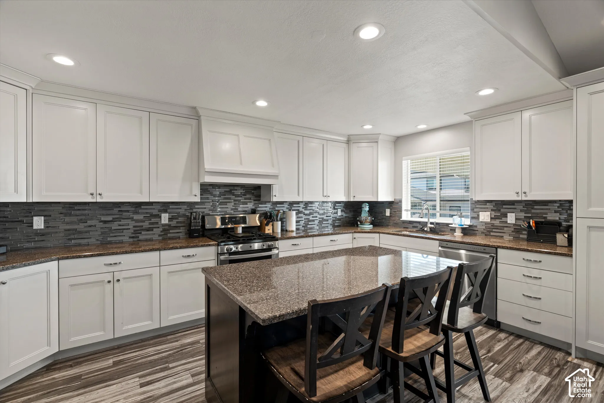 Kitchen featuring white cabinetry, stone countertops, a tile backsplash, wood-finish flooring, and recessed lighting