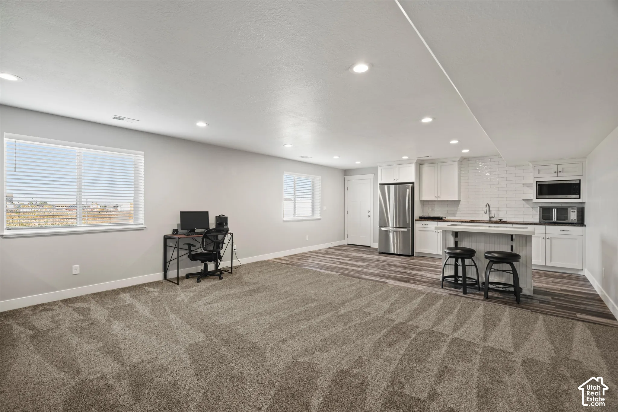 Recessed lighting throughout, two windows with blinds, wood-finish flooring, white subway tile backsplash, and stainless steel refrigerator
