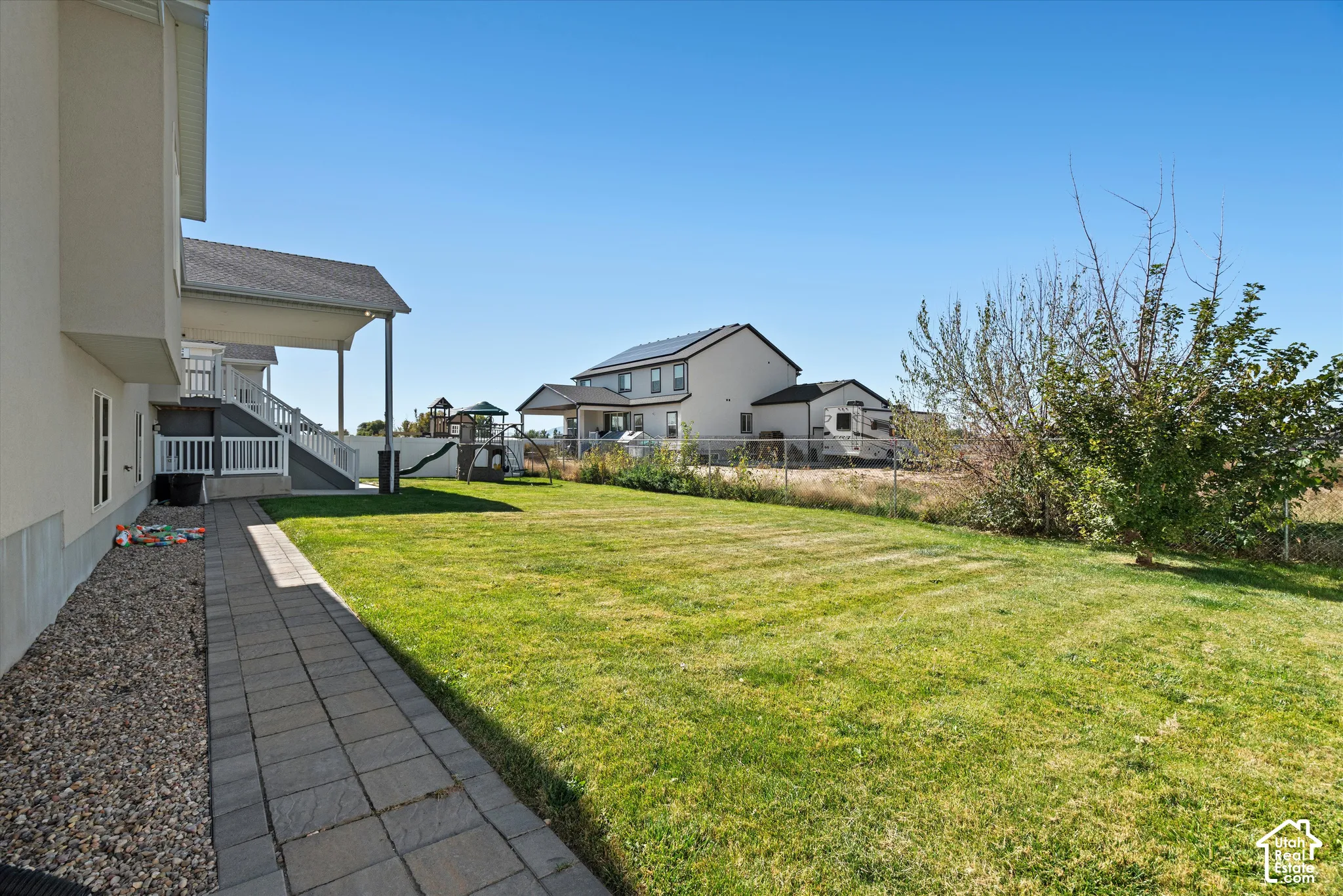 Expansive lawn area with a paver walkway, gravel landscaping, and a covered patio structure