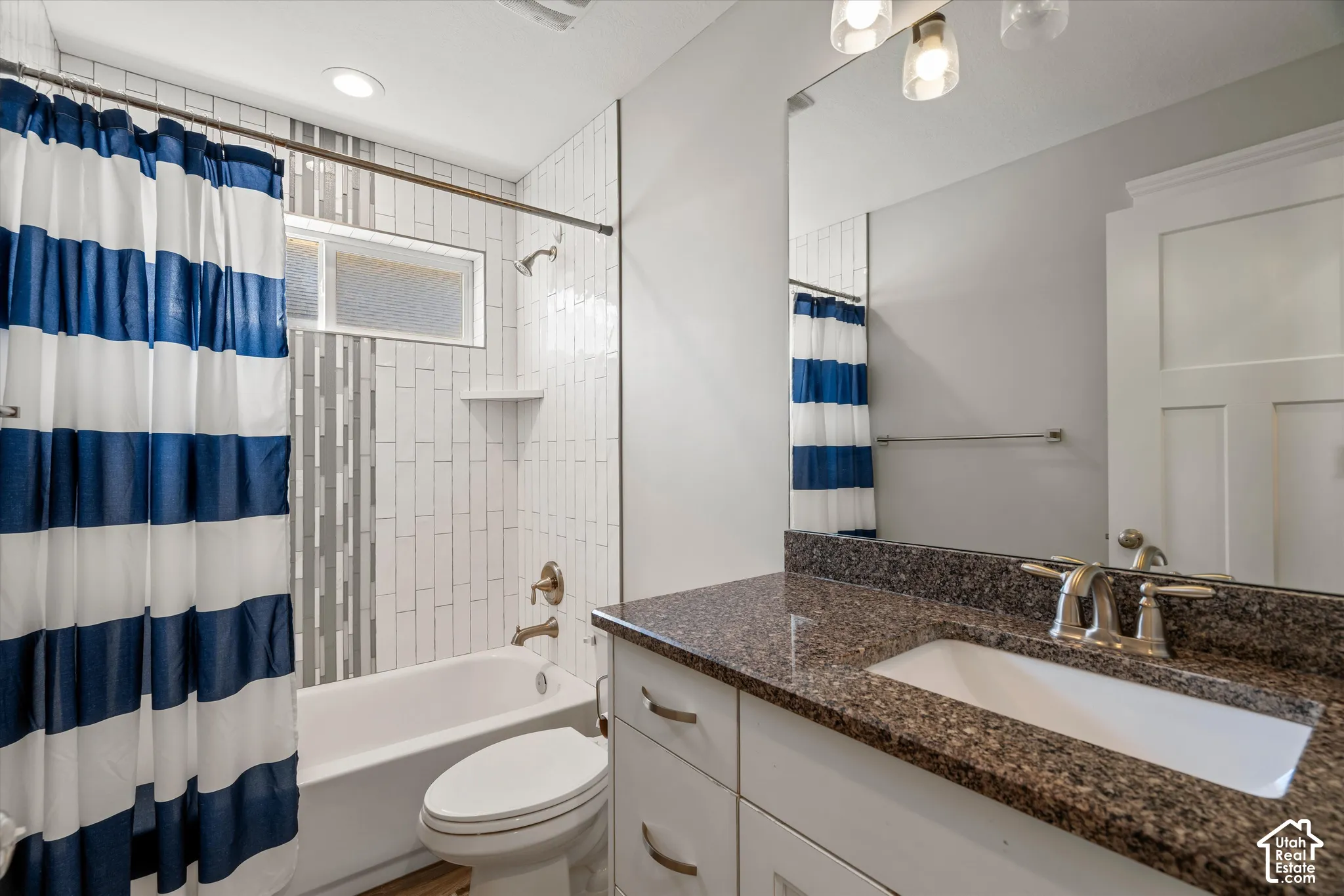 Recessed bathtub with subway tile surround, integrated shower niche, frosted transom window, and an expansive vanity with a granite countertop and undermount sink