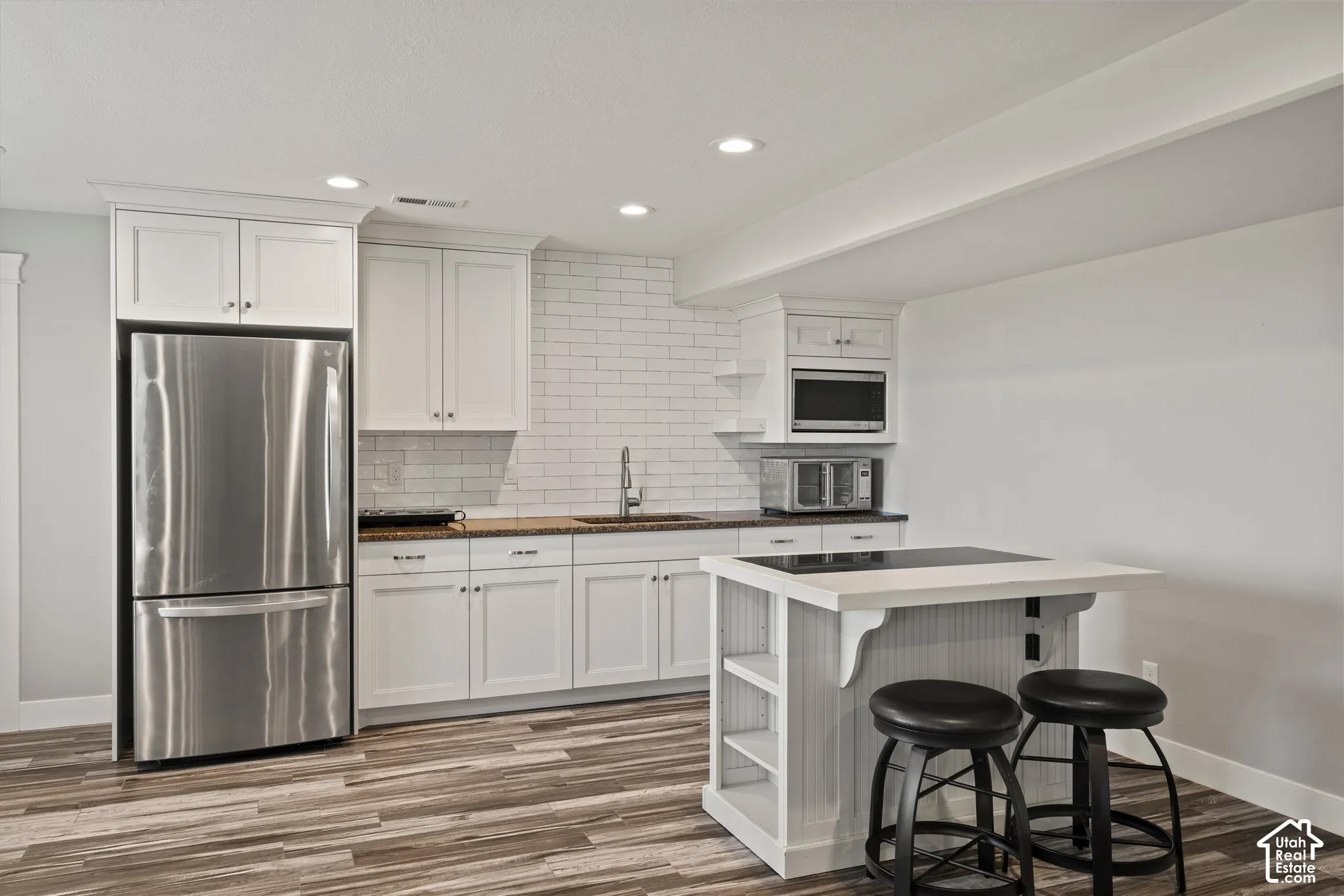 Full kitchen featuring white cabinetry, stainless steel refrigerator, white subway tile backsplash, and wood-finish flooring
